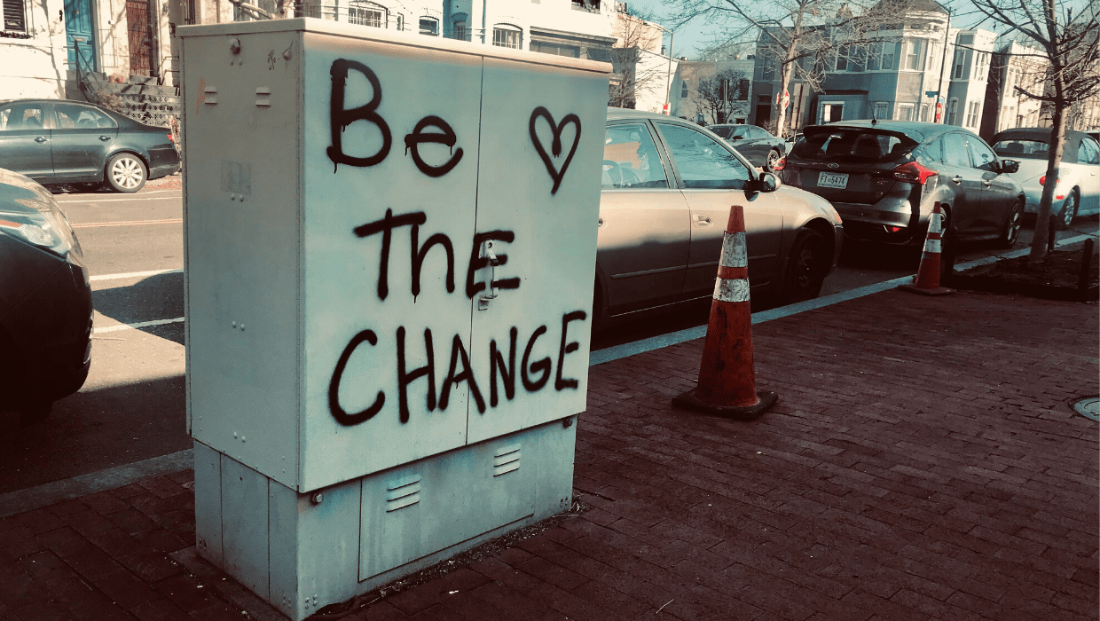 Electric box on city street with words "Be the Change" spray painted in black