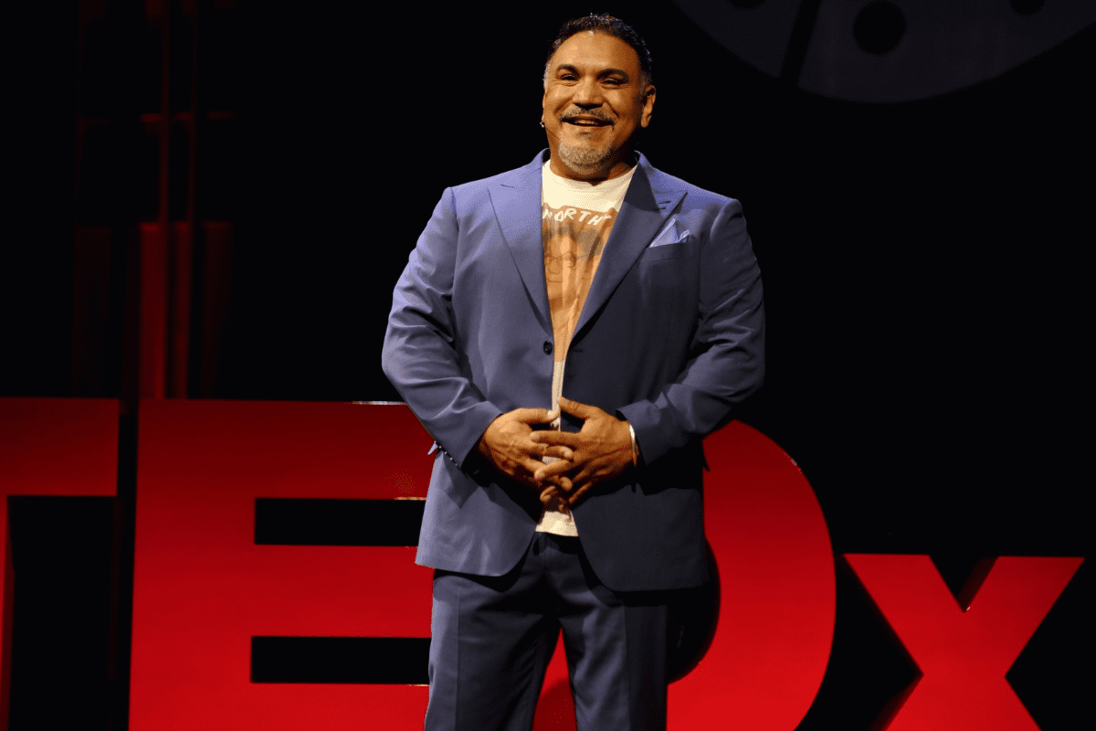 Man stands on stage with smile and hands clasped